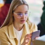 Young bespectacled blonde woman looking at her phone with some concern.