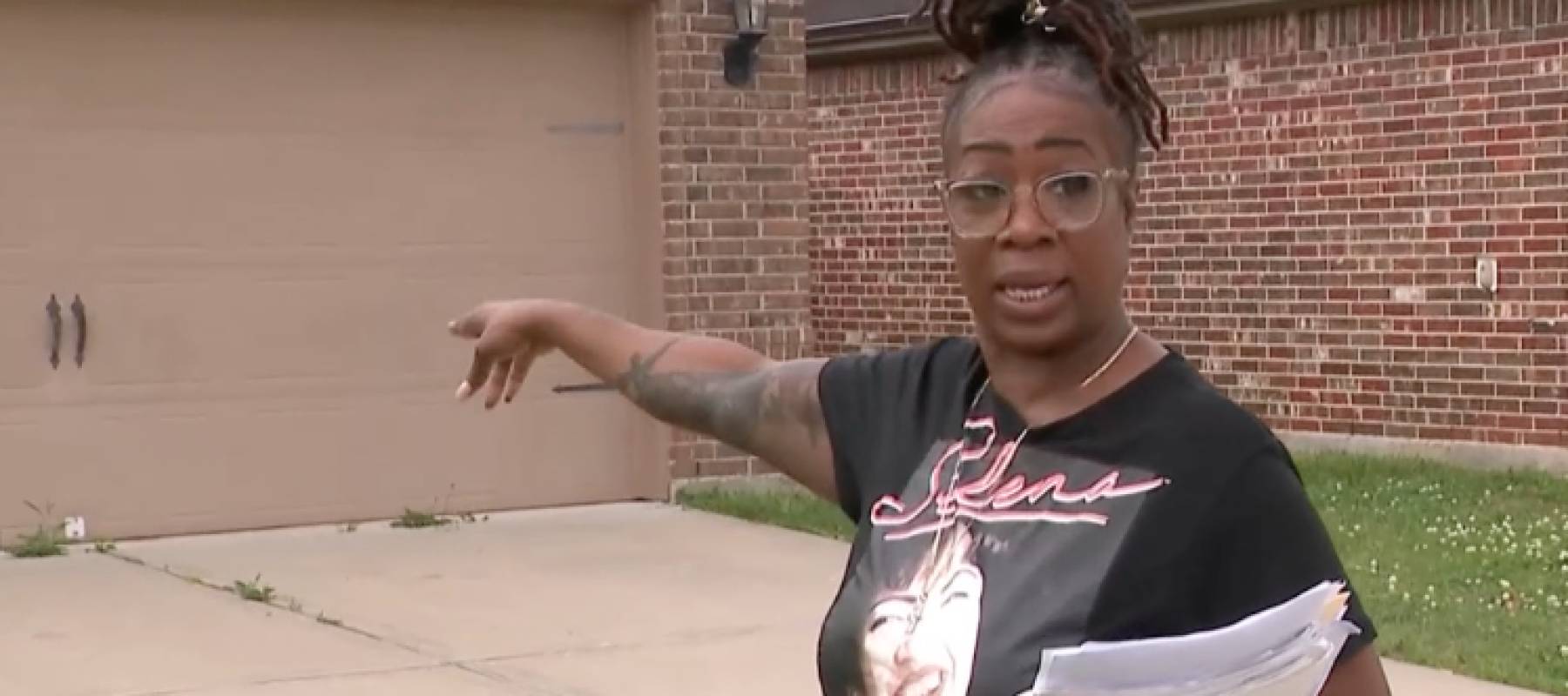 Woman holding papers pointing at house.