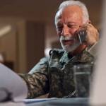 Happy mature veteran in army uniform communicating on cell phone while doing paperwork in the office.