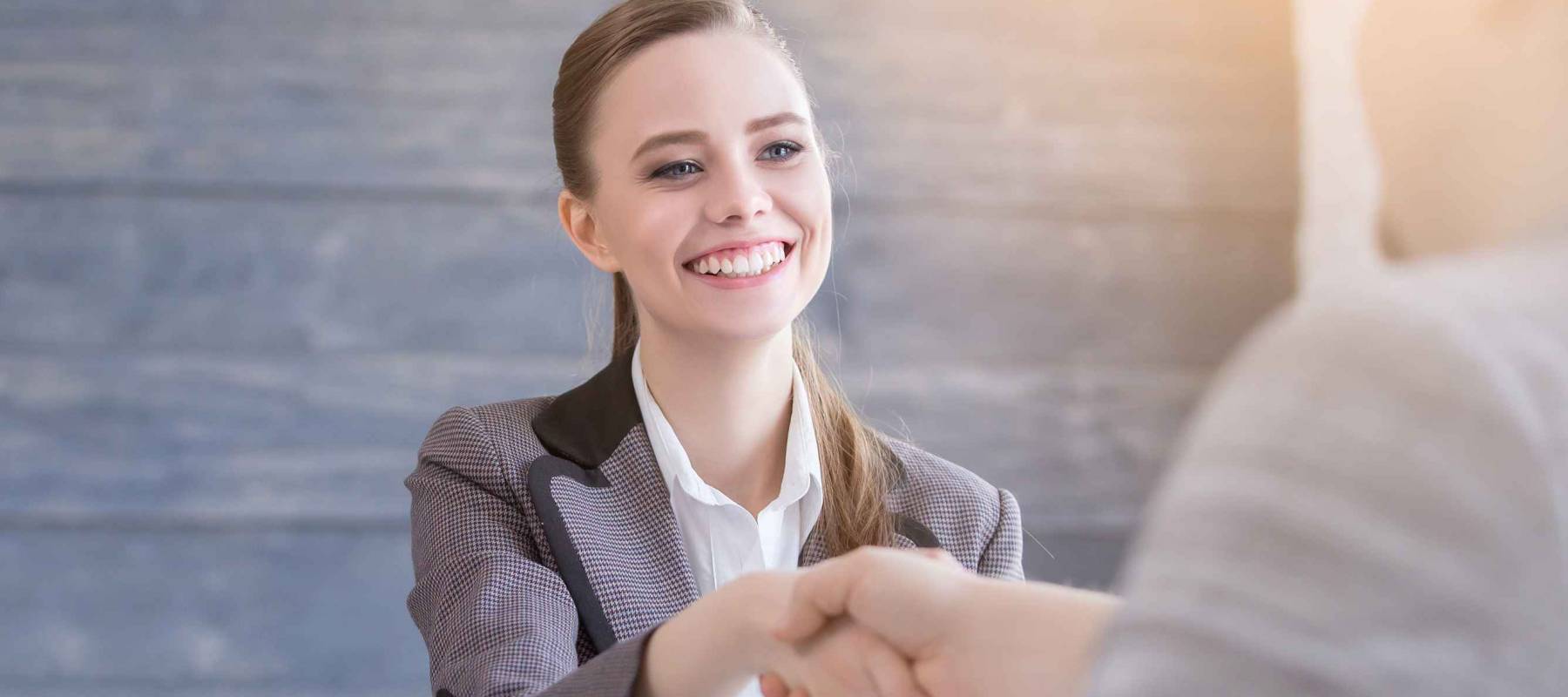 Young woman arriving for a job interview. Business people handshake in modern office. Greeting deal concept