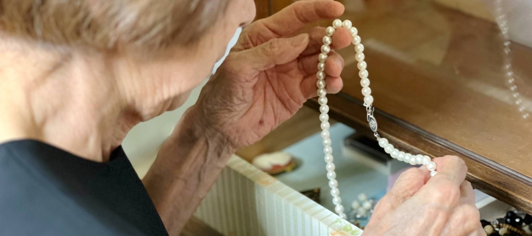Elderly woman in mourning dress taking out pearl necklace from drawer