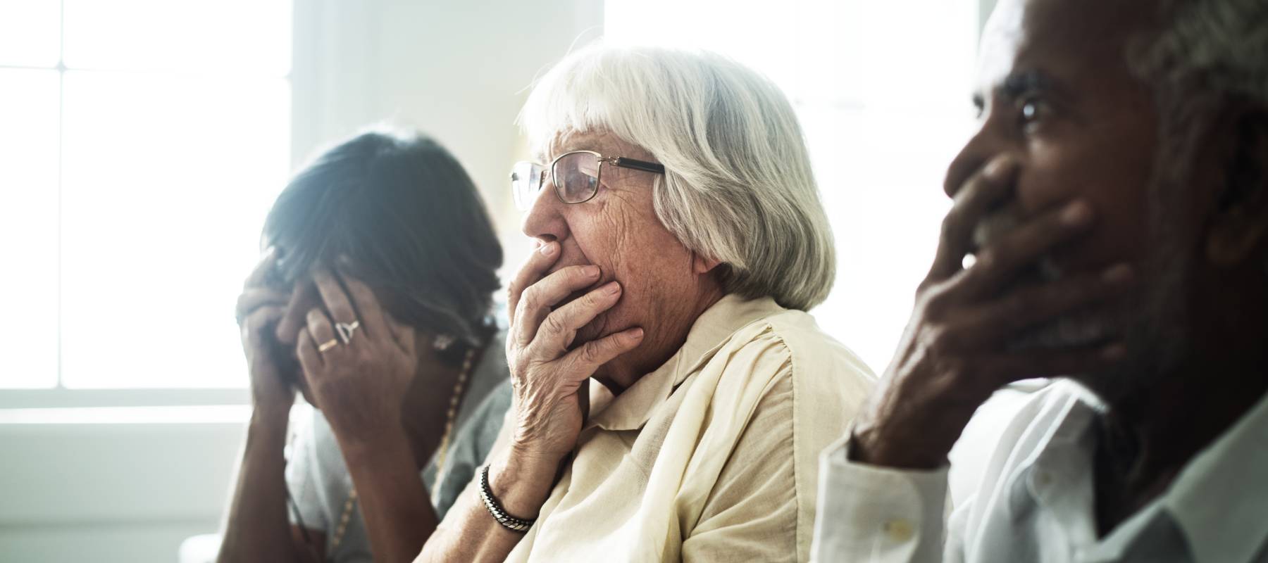 Older people sitting in a room looking shocked and concerned