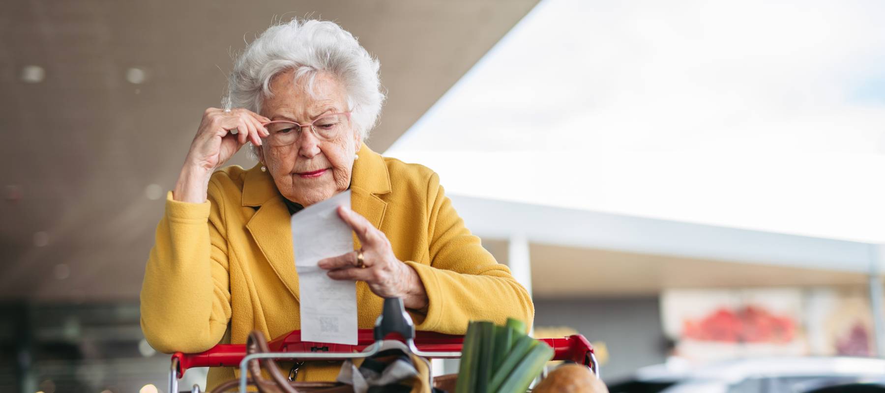Older woman checking her receipt after purchase at the grocery store, pushing a cart.