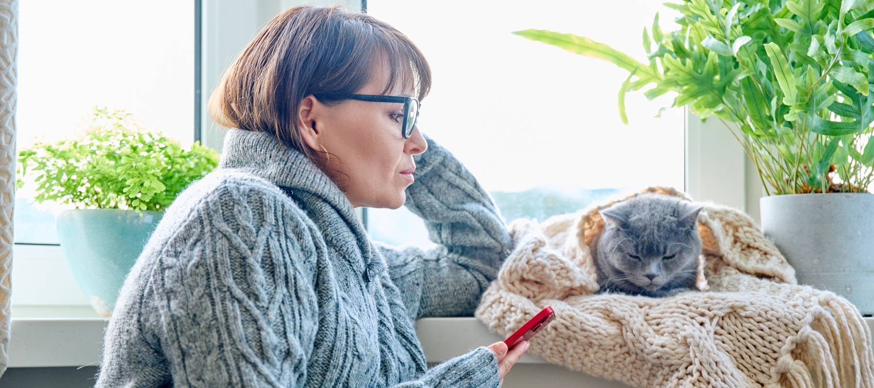 Woman looking at phone with her grey cat next to her