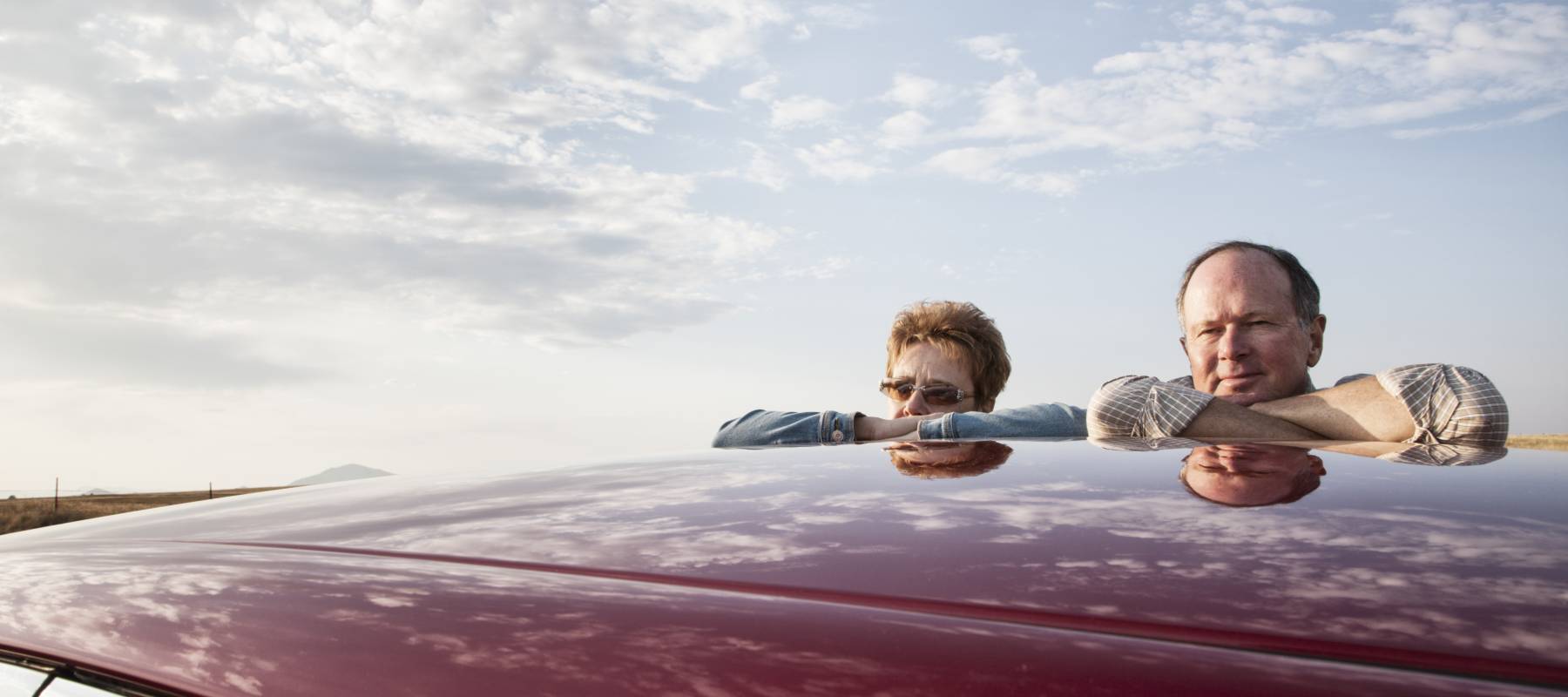 Portrait of a Caucasian senior couple leaning on their car at a rest stop on a road trip.