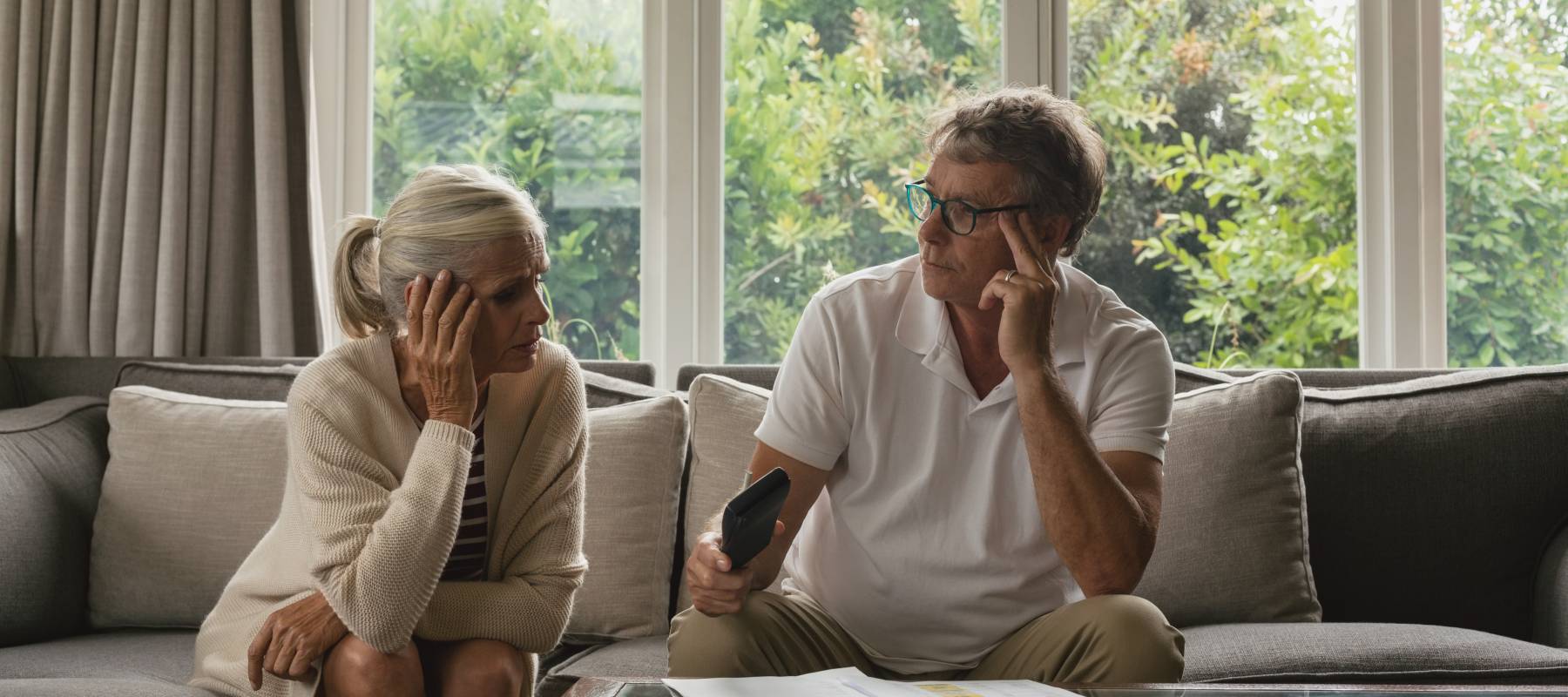 An older couple sit disturbed on a couch.