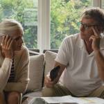 An older couple sit disturbed on a couch.