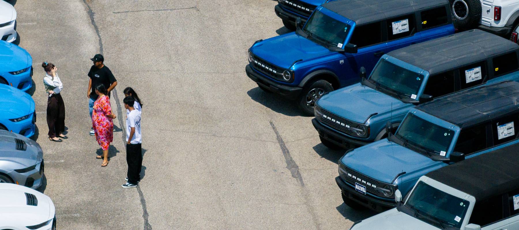 A group of people talking on a Ford car lot.