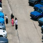 A group of people talking on a Ford car lot.