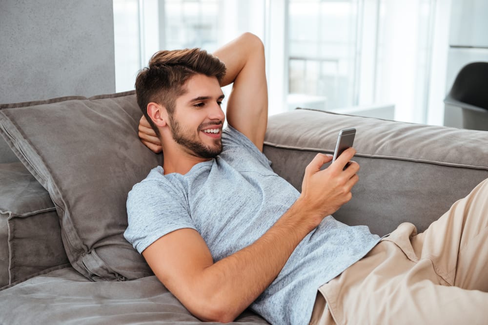 a young man lying on the couch looking at his cellphone