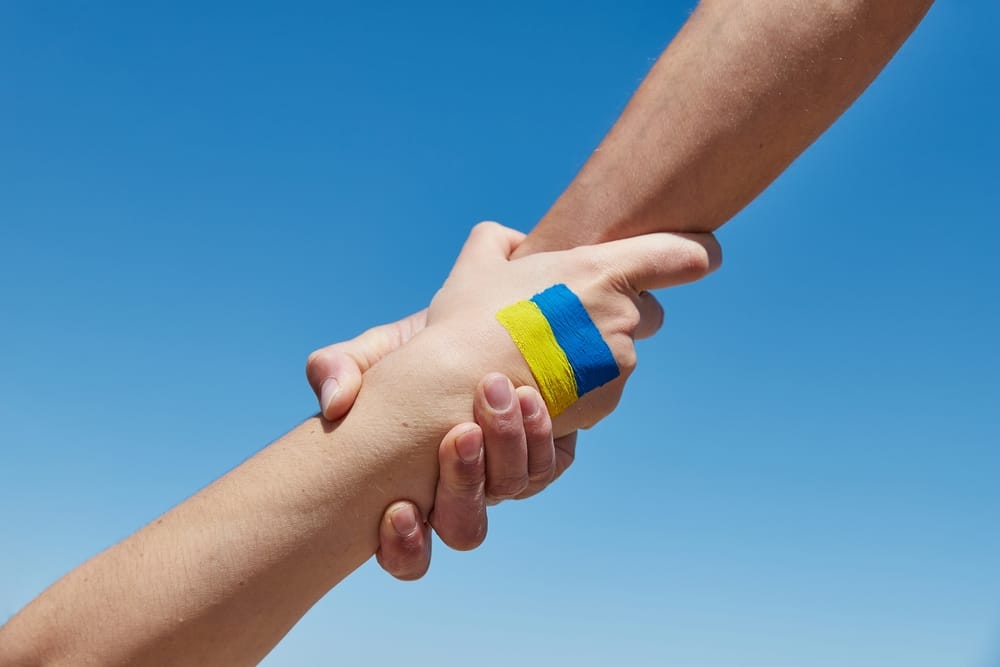 two hands clasping at the wrist with Ukrainian flag painted on one hand