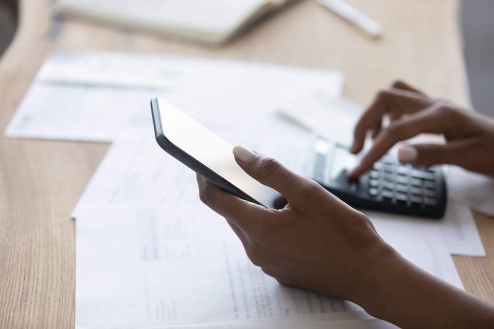 Close up young african american biracial woman holding smartphone in hands, calculating domestic expenses or bills, managing medical or financial investments using mobile e-banking application.