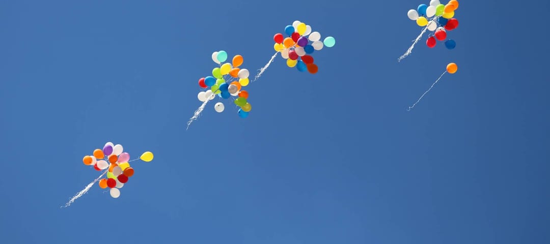 Bouquets of balloons rising against a blue sky.