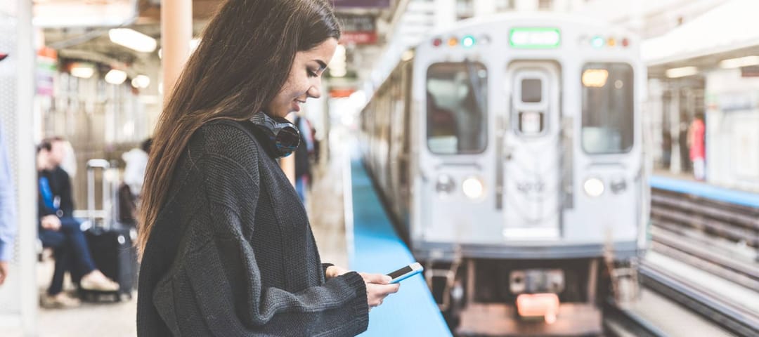 Girl with smart phone at train station in Chicago. Portrait of a young woman, mixed race, looking at the phone while waiting for the train on the platform
