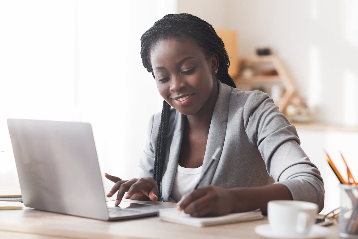 Black female entrepreneur working in office, typing on laptop computer and taking notes, free space