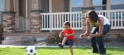 Mother and son in front yard playing with soccer ball