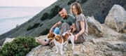 A young couple taking a break from hiking with their dog along the rocky shoreline