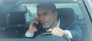 Close up view of stressed middle aged man in a car talking on phone while driving.