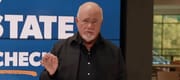 Dave Ramsey speaks in front of a large screen on a television set.