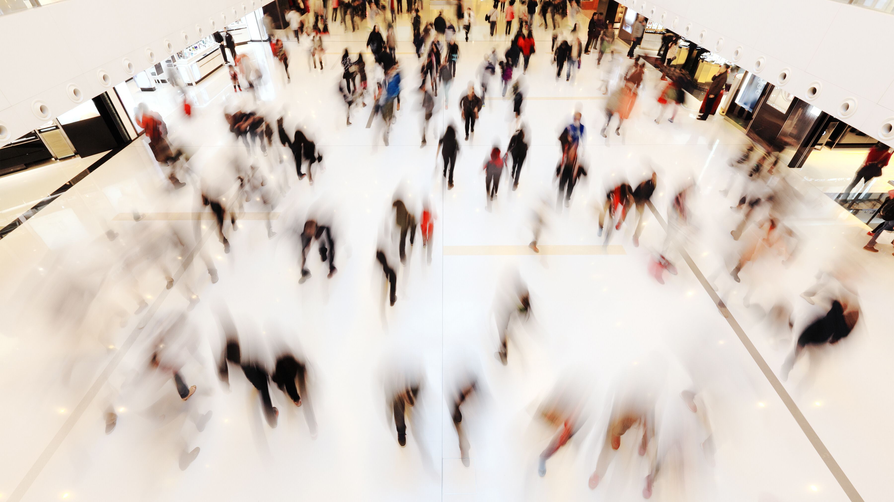 Crowds of people mill about in a shopping mall, blurred out