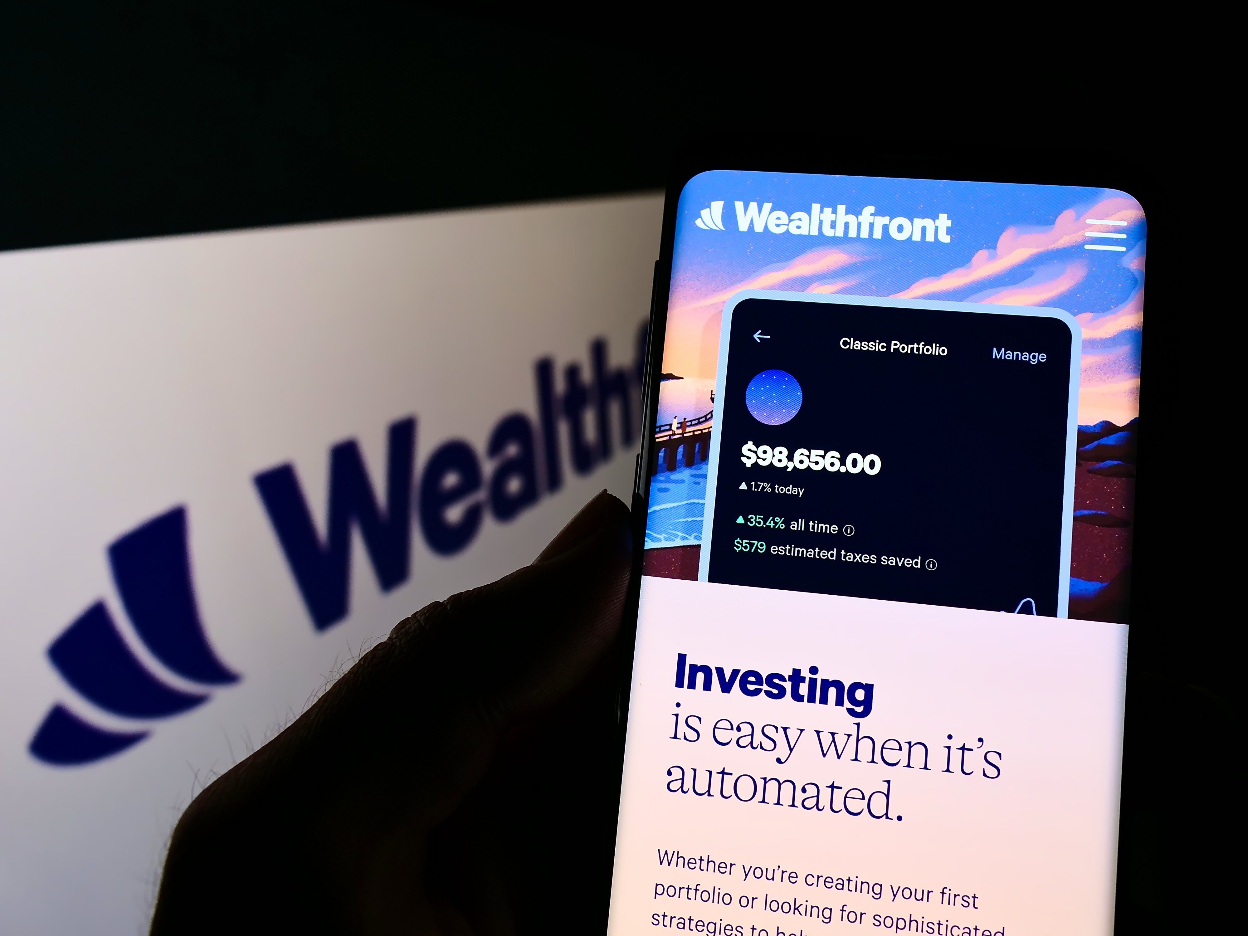 Person holding cellphone with website of US fintech company Wealthfront Corporation on screen in front of logo. Focus on center of phone display.