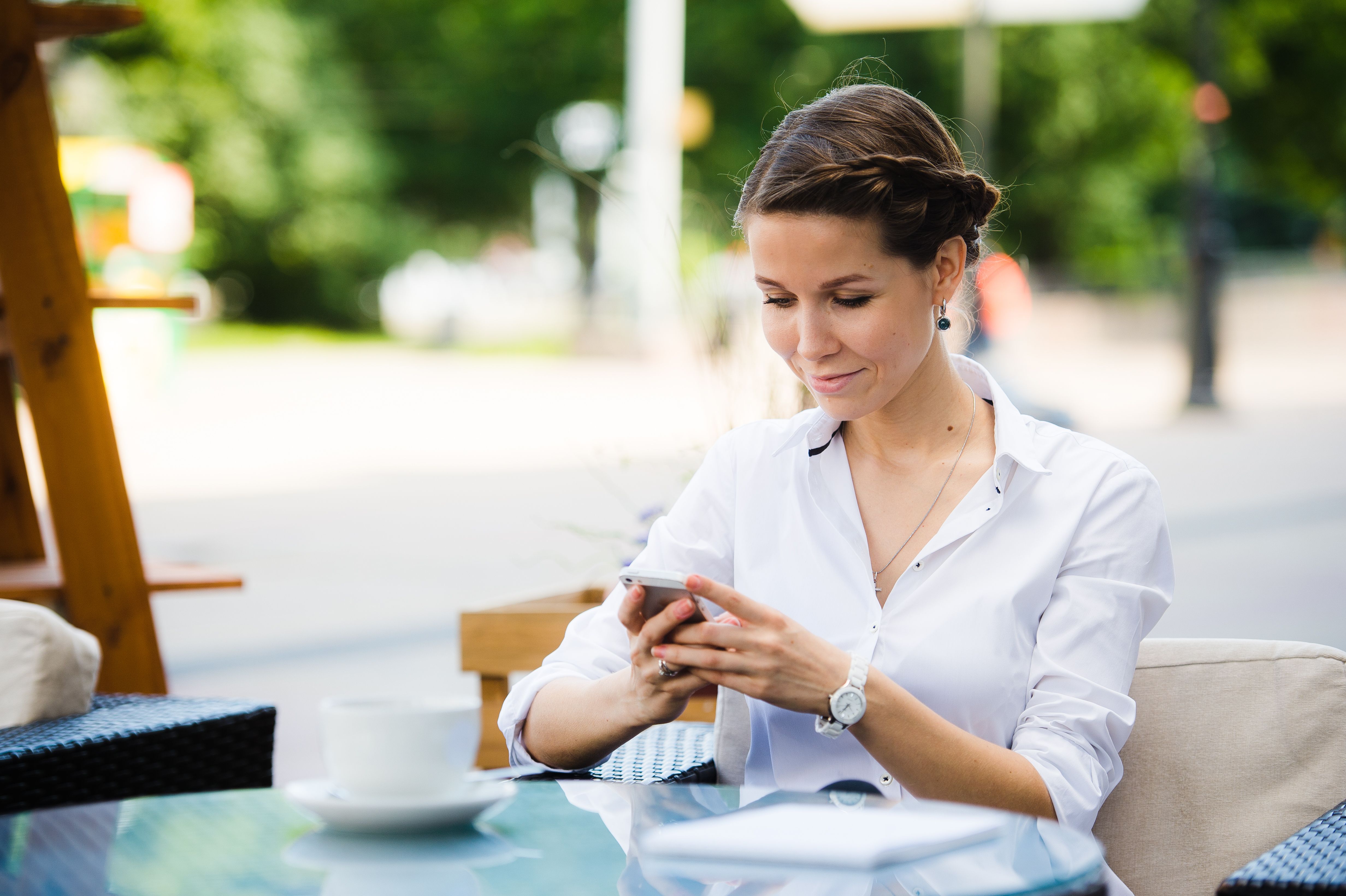 Portrait of a charming business woman chatting on her smart phone while waiting someone in cafe outdoors,