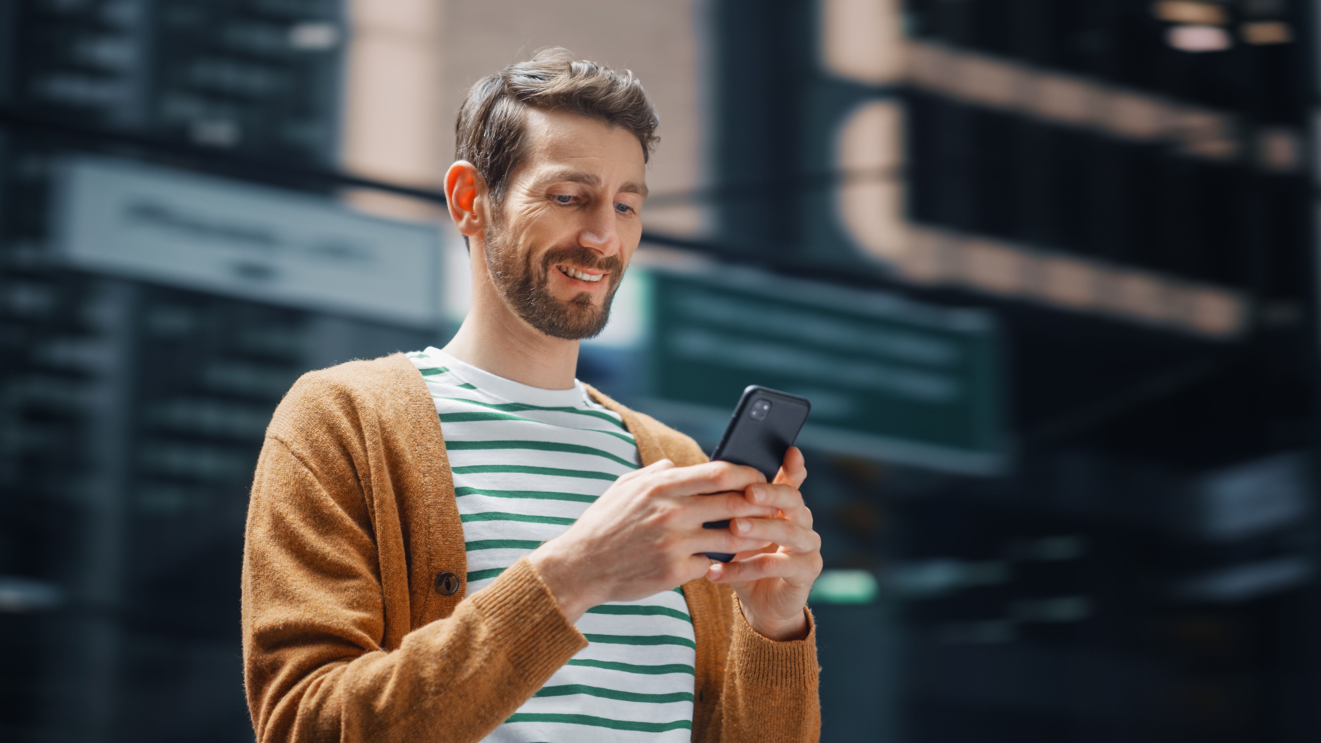 Street Shot: Portrait of Caucasian Man Using Smartphone in the Big City. Creative Professional Using Mobile Phone App for e-Commerce Online Shopping. Blurred Background.