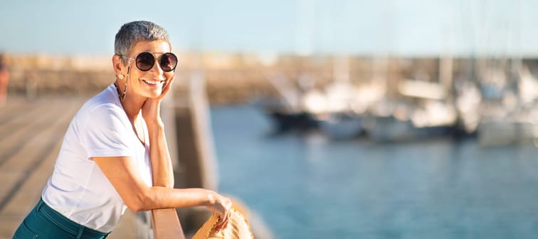 Youthful retiree with cropped hair and large round sunglasses staring out into the marina with a smile on her face.