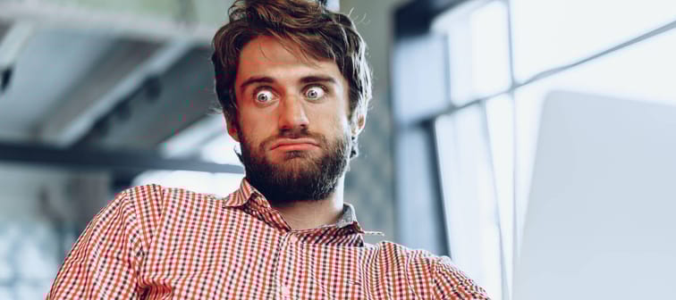 Man with beard sitting in front of a laptop looking perplexed