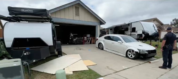 A police officer stands in front of a house with two trailers.