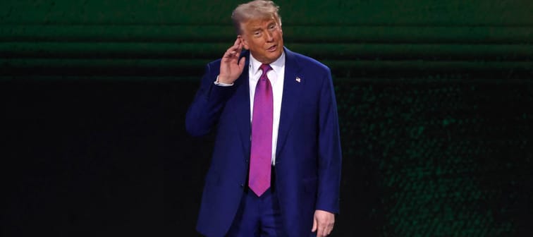 Donal Trump holds his hand to his ear on stage.