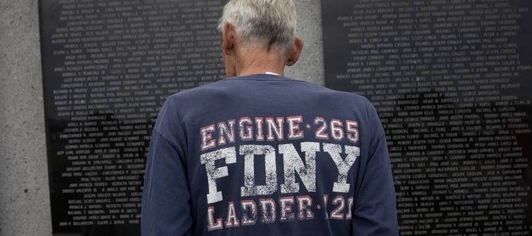 A man wearing an FDNY  t-shirt satnds in front of a 9/11 memorial.