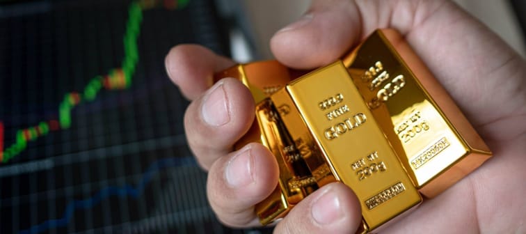 Hand holding gold bar and phone that opens the candlestick chart. and dollar.