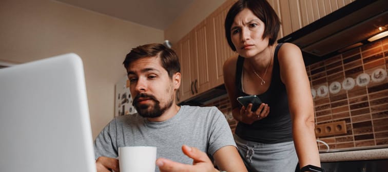Couple at kitchen, reading news and using laptop.