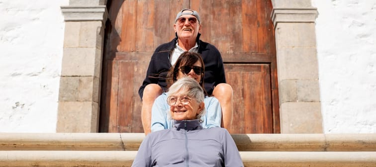 Group of senior friends sitting outdoors on the steps in front of an old wooden church door.