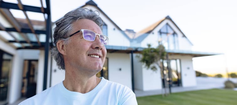 An older man looks into the distance outside his home.