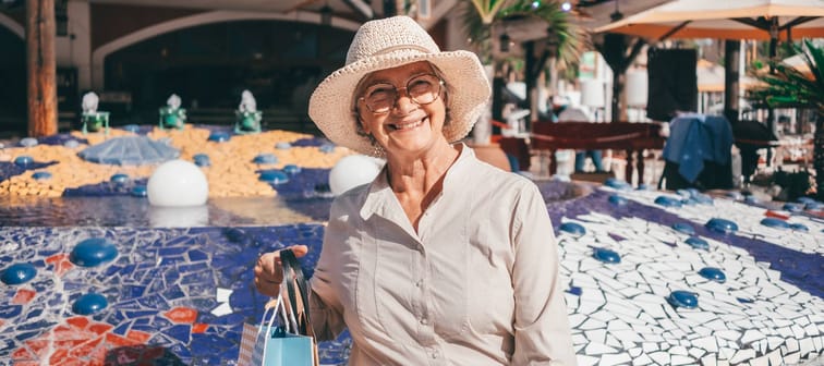Happy senior woman sitting outdoors with shopping bags