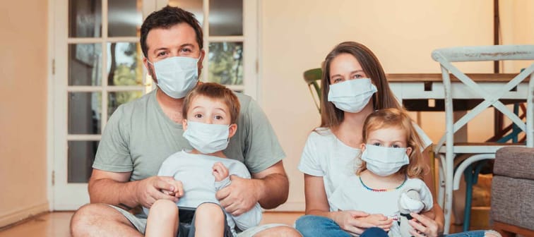 Beautiful young family wearing face masks against coronavirus world pandemic and staying home