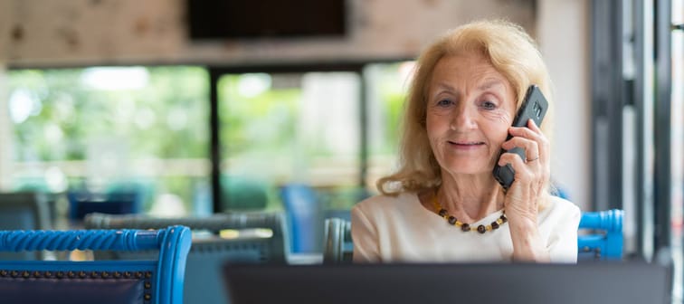 Happy senior woman smiling and using laptop computer while talking on phone