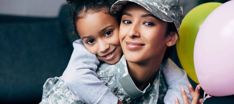 african american daughter hugging her mother in military uniform with balloons at home