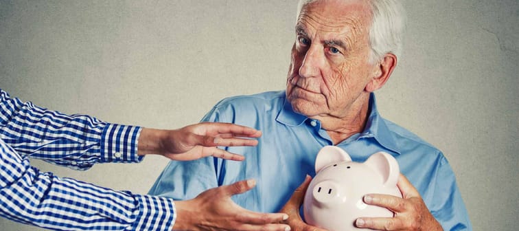Closeup portrait senior man grandfather holding piggy bank looking suspicious trying to protect his savings from being stolen isolated on gray wall background. Financial fraud concept