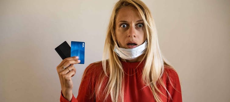 A blond girl wears a protective medical mask, holds a credit card, on a beige background. The concept of quarantine, coronavirus, shopping. shock, credit, no have money, work after quarantine