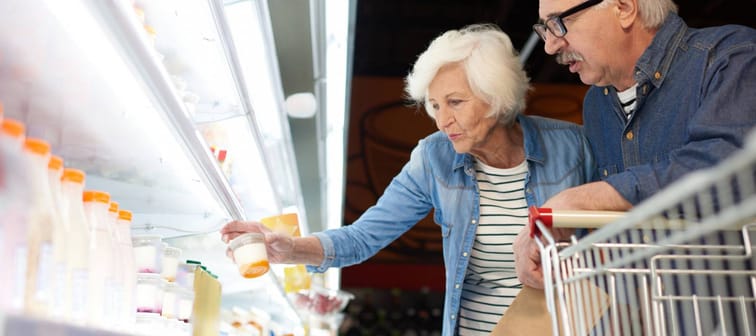 Side view portrait of modern senior couple choosing milk products standing by dairy isle in supermarket while grocery shopping, copy space