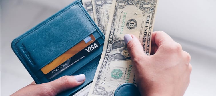 Hands putting U.S. dollar bills into a blue wallet
