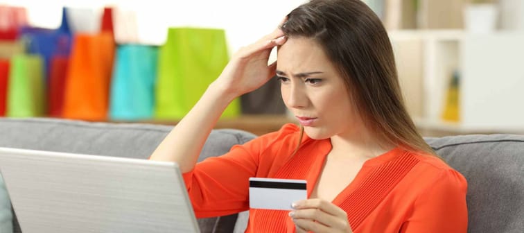 Worried shopper buying online with credit card sitting on a couch in the living room at home