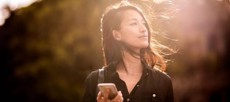 Young Asian-American woman holding cellphone in the sun