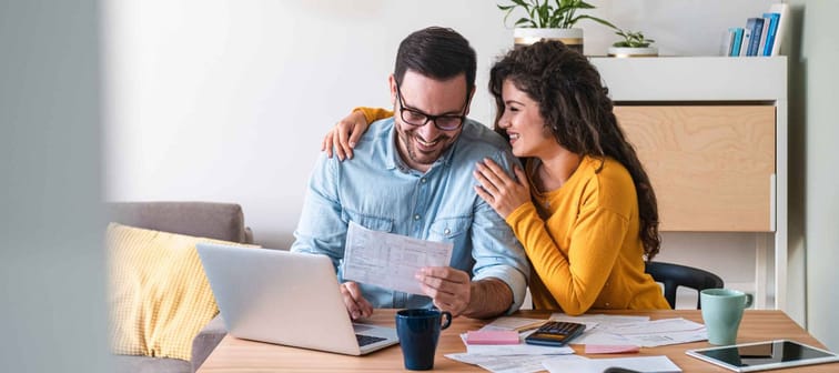 Positive young couple embracing and paying household bills or taxes on laptop online at home stock photo