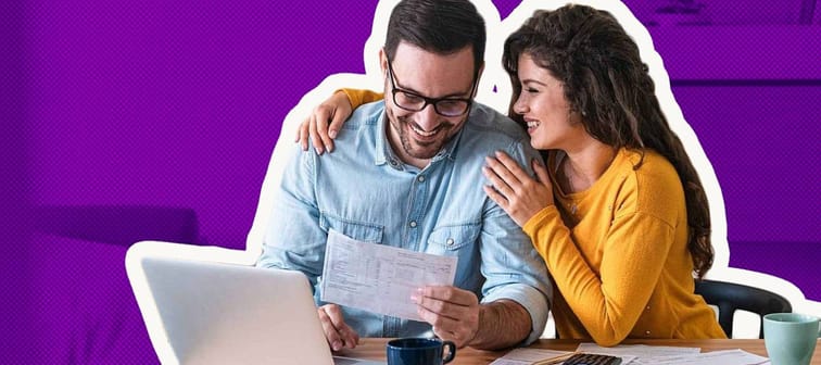 Positive young couple embracing and paying household bills or taxes on laptop online at home