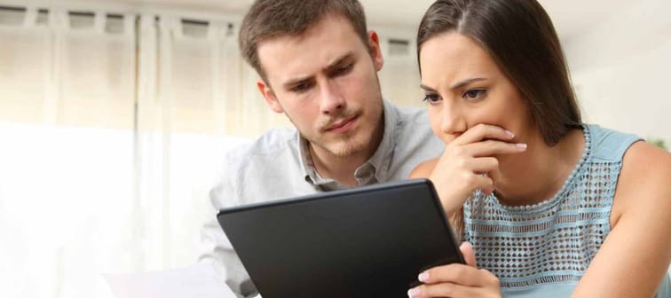 Concerned looking couple look at tablet and papers, woman has hand over her mouth