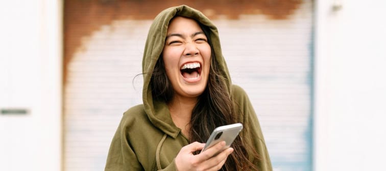 Young Asian-American woman in green hoodie is ecstatic over something on her smartphone